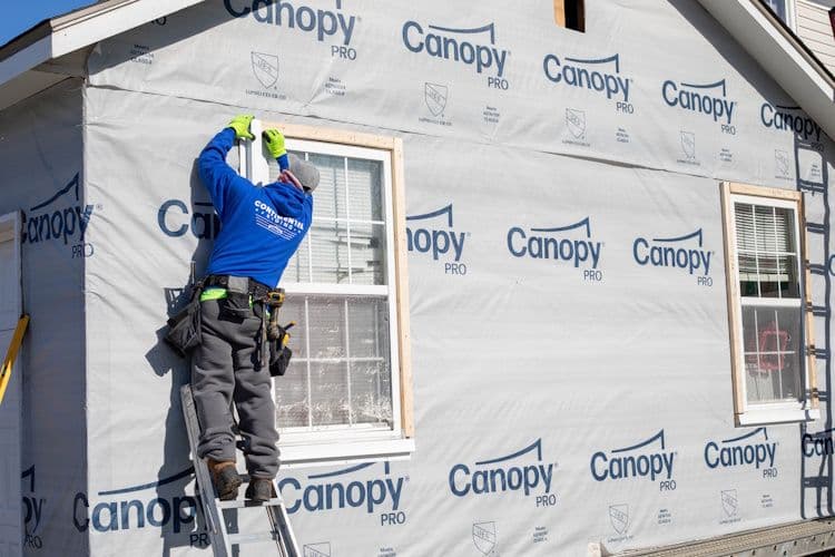 Worker in blue shirt installing weather barrier on house exterior covered with Canopy Pro brand wrapping