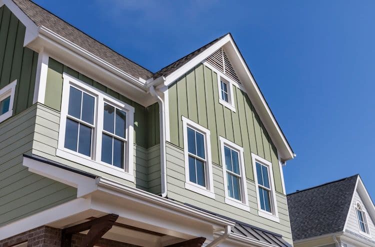 Two-story green and white house with white-trimmed windows and gabled roof against clear blue sky