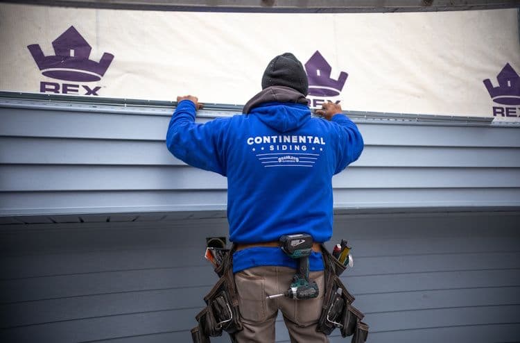 Worker in blue Continental Siding jacket installing siding on home exterior with REX brand trim visible